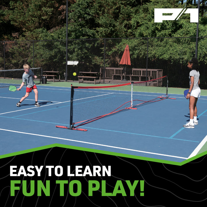 Two children playing pickleball on blue court with portable net and P1 paddles, trees and benches in background