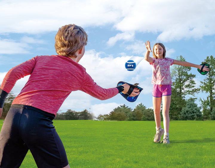 Two children playing Toss & Catch Ball Game outdoors on green grass with blue sky and trees in background