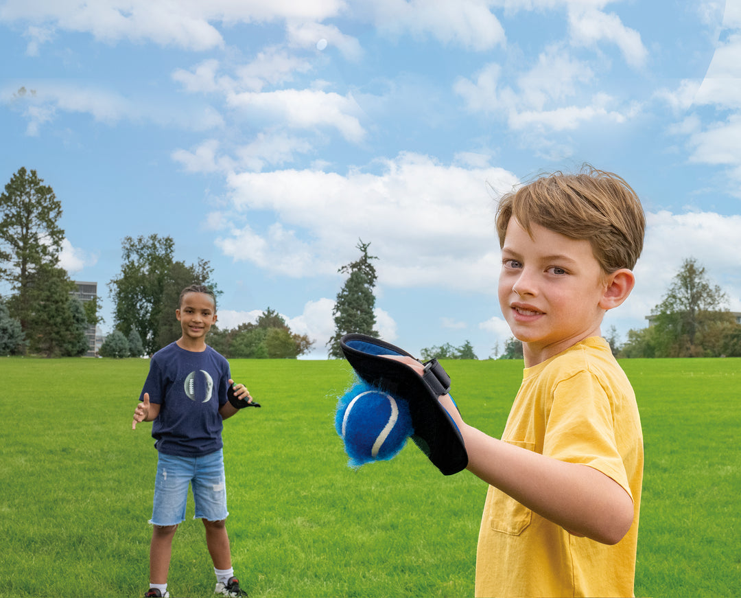 Two boys playing Toss & Catch Ball Game outdoors on green grass under blue sky with scattered clouds