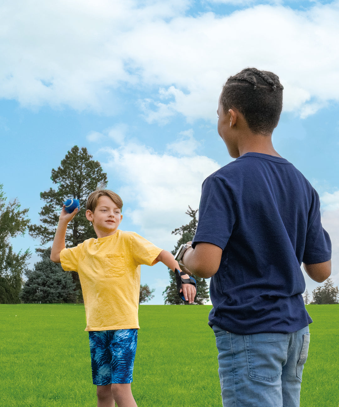 Two boys playing Toss & Catch Ball Game outdoors on green grass with blue sky and trees in background