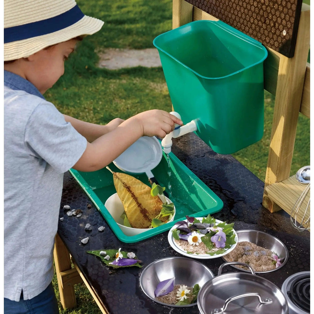 Little boy engaged in outdoor sensory play using a wooden mud kitchen set.